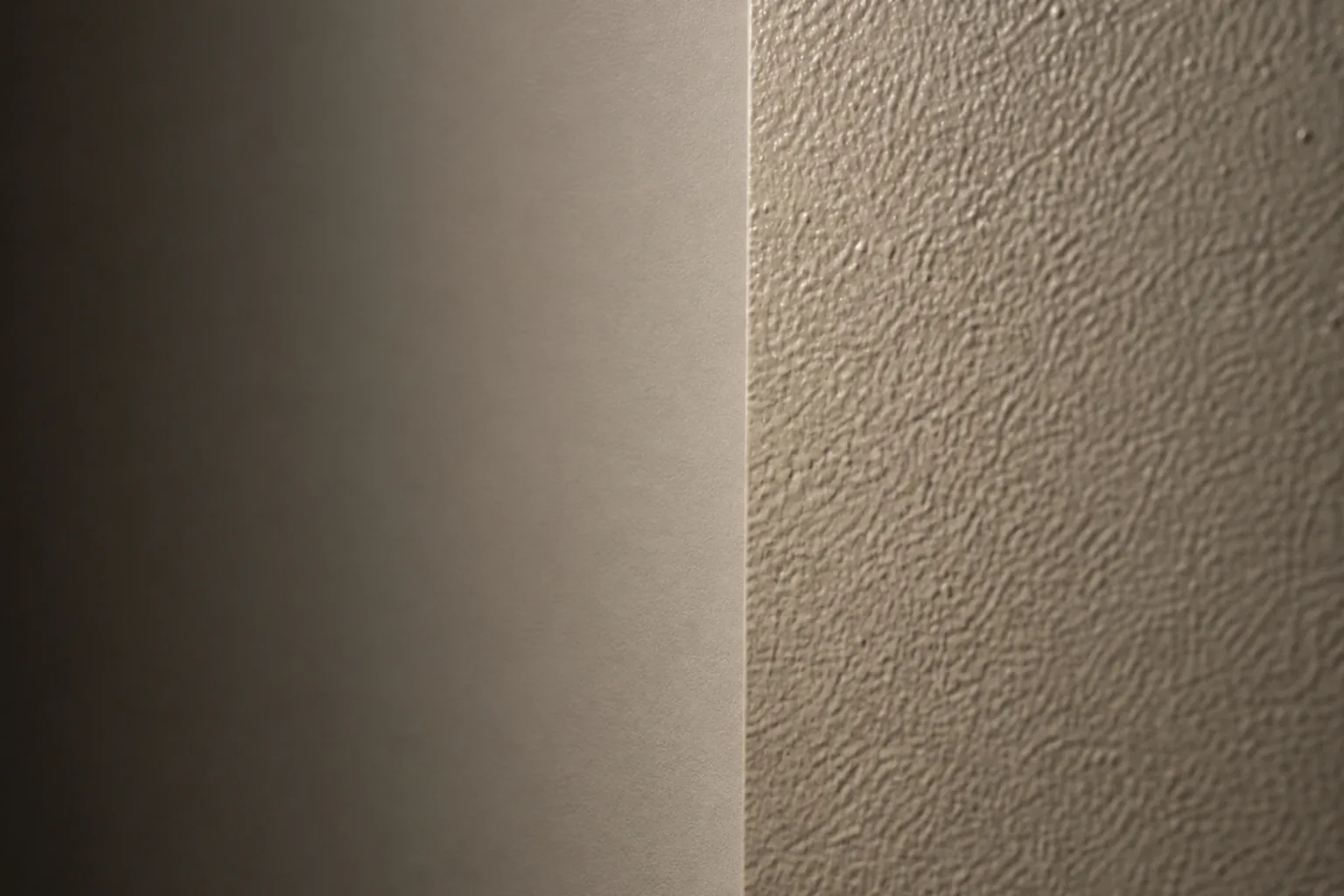 Close view of a smooth painted wall beside a textured plaster wall in raking light