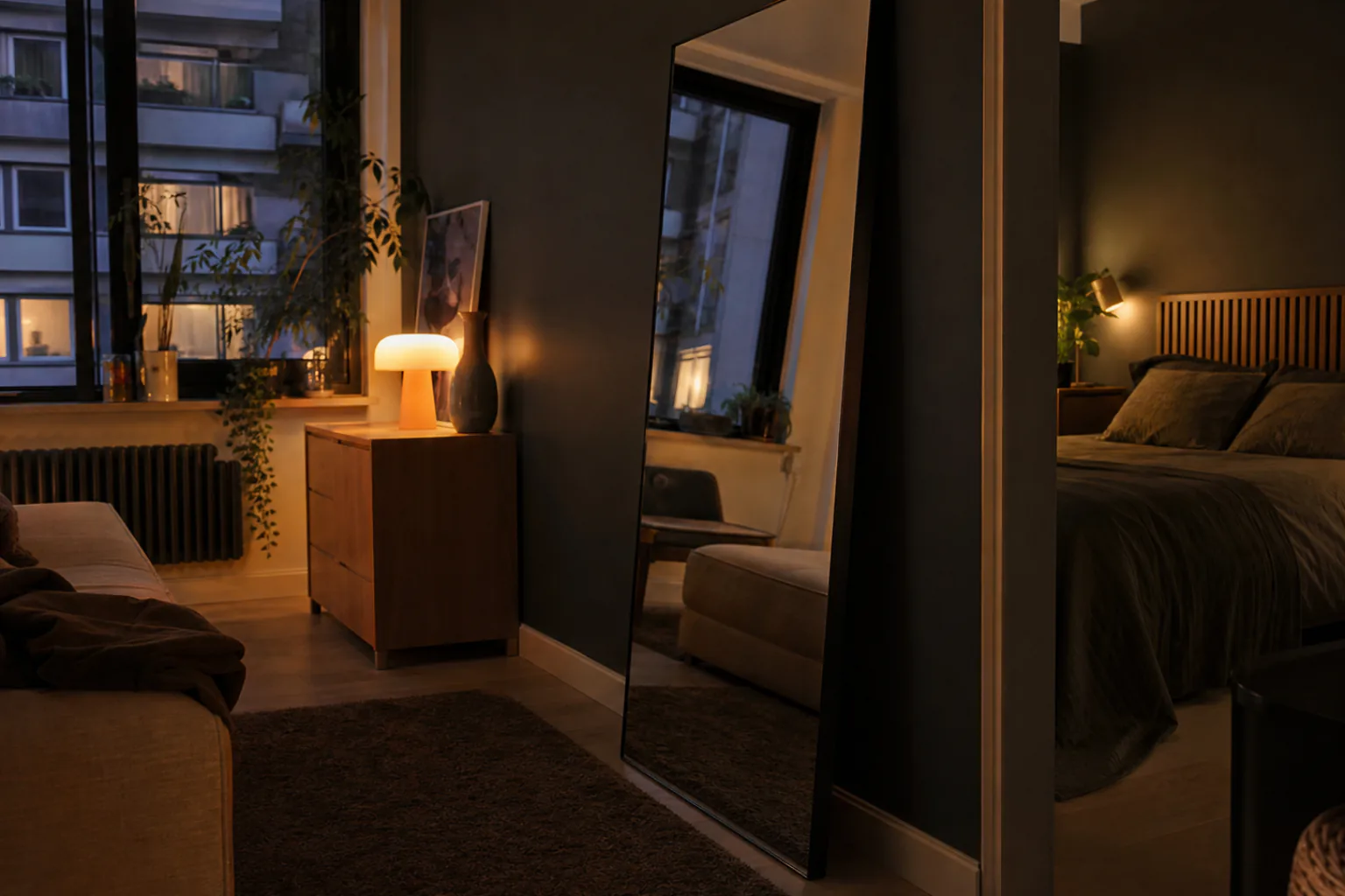 Tall mirror leaning against a wall reflecting warm lamplight in a small apartment